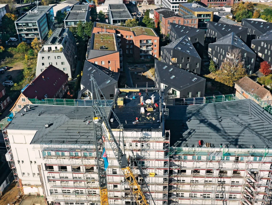 Großbaustelle mit laufenden Flachdach-Abdichtungsarbeiten und Baukran, Drohnenaufnahme